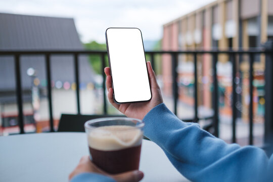 Mockup image of a woman holding and using mobile phone with blank desktop screen while drinking coffee in cafe