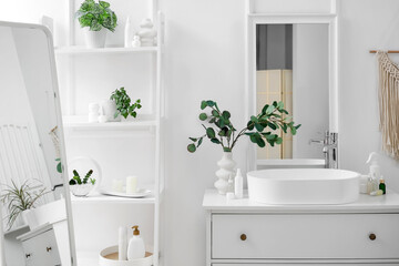 Fototapeta premium Interior of light bathroom with chest of drawers, sink and shelving unit