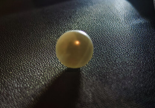a pearl-like object placed on a dark textured surface with dramatic lighting and detailed material texture. Suitable for luxury design, jewelry concepts, beauty products, premium backgrounds, abstract