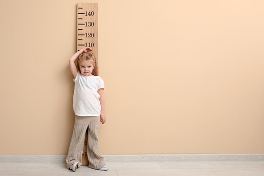 Cute little girl measuring height near beige wall