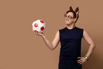 Portrait of personal trainer in Christmas reindeer headband holding soccer ball on beige background © Pixel-Shot
