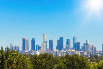 Obraz premium Modern skyline with futuristic skyscrapers glowing under bright blue sky, vibrant urban cityscape framed by lush green tropical foliage, aerial-inspired perspective