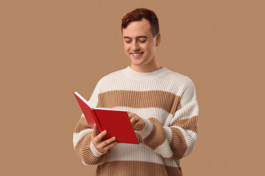 Smiling young man reading book on color background