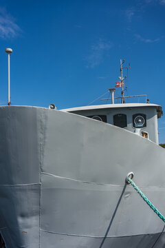 Close up of a grey ship bow docked in a harbor under a clear blue sky