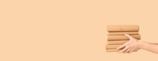 Fototapeta premium Person's hand holding a stack of books wrapped in brown paper, education and learning concept, the books are presented against a neutral beige background with ample copy space