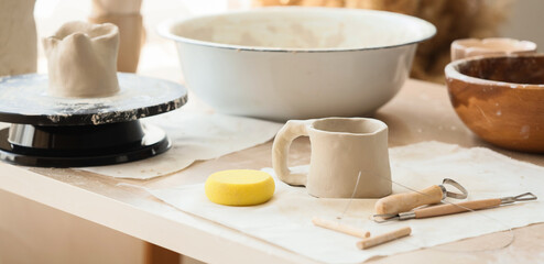 Unfinished clay mug and pottery tools on a workshop table, creative hobby and ceramic art © Pixel-Shot