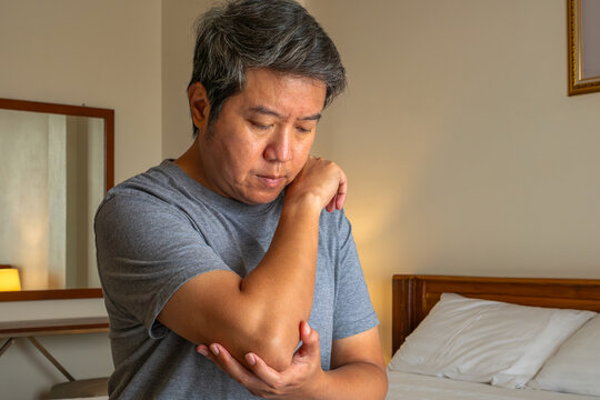 Man holding elbow in discomfort, symbolizing joint pain and medical treatment focus.