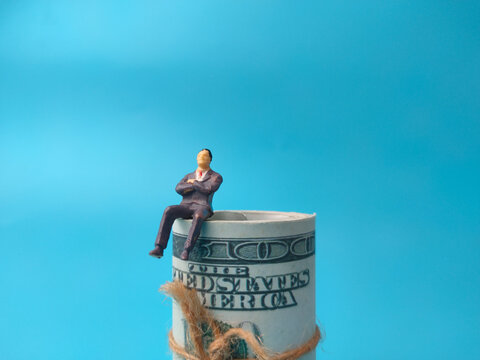 A miniature businessman figure sitting atop a tightly rolled roll of United States dollar bills