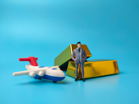 A miniature businessman figure sitting on stacked toy gold bullion bars over a plain blue background