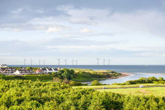 Scenic coastal landscape with offshore wind turbines, green countryside, seaside homes and dramatic clouds along the North Sea coast near Aberdeen, Scotland