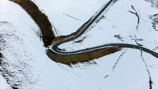 Aerial View of a Red Car Driving on a Winding Road Through Snowy Mountains with Traditional Yurts