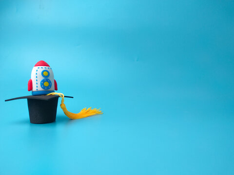 A toy rocket standing on top of a miniature black graduation cap with a yellow tassel