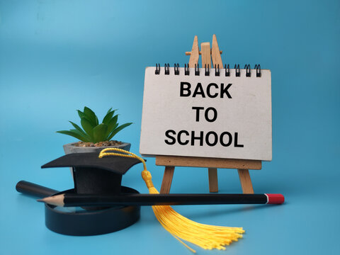 A small easel displaying BACK TO SCHOOL text alongside a miniature graduation cap, pencil, plant, and magnifying glass