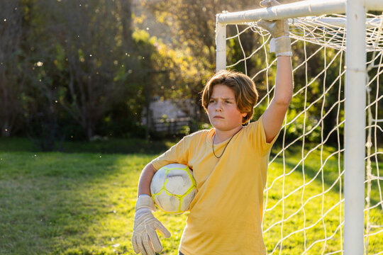 portrait of teenage boy holding soccer ball at sunset