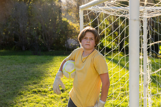 portrait of teenage boy holding soccer ball at sunset