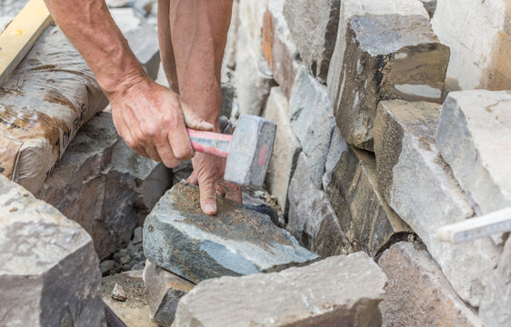 Building a brick wall of natural stone, with hammer, handmade, close-up of human hands