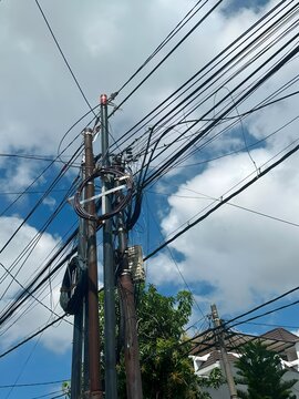 Utility Pole with Overhead Fiber Optic and Power Cables Against a Blue Sky with Dramatic Clouds