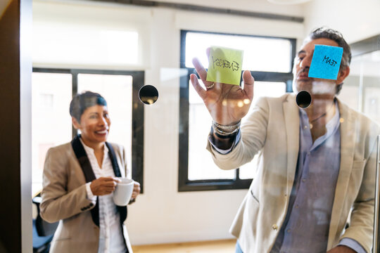 Professionals working on a project, applying sticky notes with concepts energy and team to a transparent wall in an office