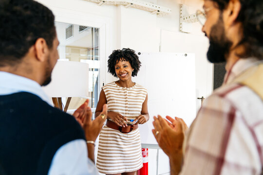 Diverse business professionals in a coworking space applauding a smiling woman after her presentation, celebrating success and collaboration