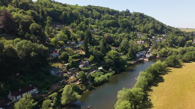 Drone aerial view of the River Wye winding through the picturesque village of Symonds Yat near Ross-on-Wye, surrounded by woodland, riverside cottages, rolling hills and golden summer fields, with kay
