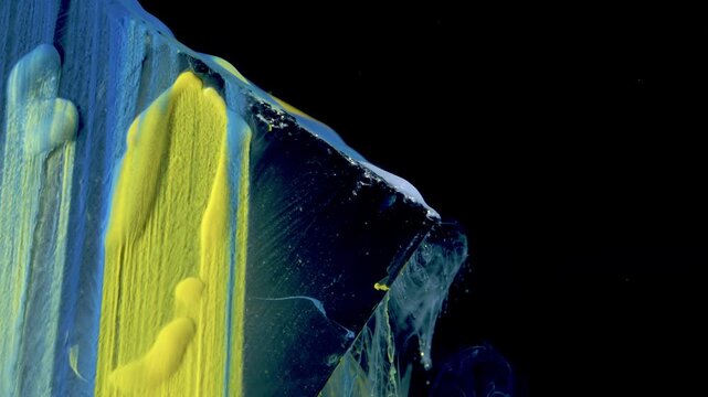 Tight oblique close-up of thick blue and yellow paint layered on transparent sheet, showing viscous ridges, bulbous drips, and pulled gel filaments along torn diagonal