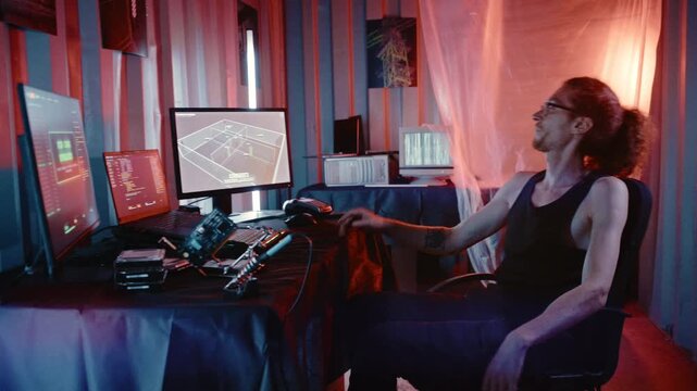A long-haired computer specialist relaxes inside a neon-lit container workspace after completing a demanding digital task.