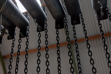 Naklejka premium Rows of heavy black steel chains hang in an industrial hall, an abstract repetitive metal pattern.