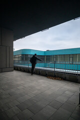 Obraz premium Man Standing on Modern Balcony Looking at Turquoise Office Building Architecture
