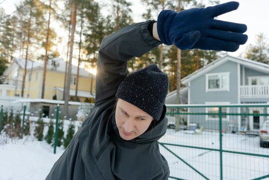 A guy in his forties does side bends with one arm raised on a frosty morning. He exercises outdoors, committed to fitness in cold weather.