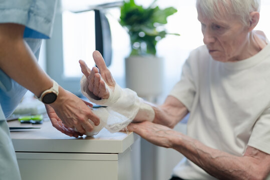 Nurse helping with bandage on elderly man in clinic. Healthcare provider assisting senior male patient with compassion and gentleness. Aging man support and elderly care in medical facility room