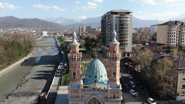 VLADIKAVKAZ, RUSSIA - APR 7, 2025: Editorial aerial view capturing the stunning Sunnite Mukhtarov Mosque on the Terek River embankment with mountain backdrop.