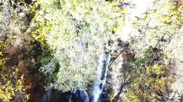 Aerial view of Keivu waterfall cascading through vibrant autumn foliage and rocky terrain in Krasnaya Polyana, Russia.