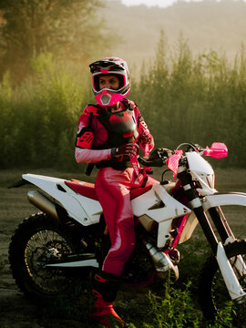 Woman in pink gear sitting on a dirt bike during a sunny morning in a grassy field