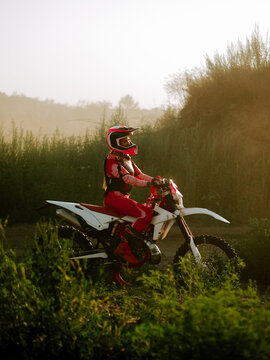 Woman in pink gear riding a white dirt bike on a hilly trail during a bright summer sunset