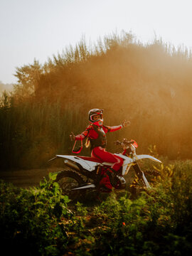 Motocross rider celebrating success on a dirt bike during sunset in a scenic outdoor rural landscape