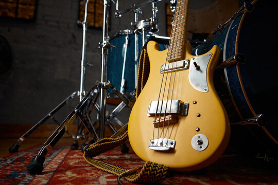 Bright yellow bass lying by drum set on decorative rug under atmospheric studio lighting