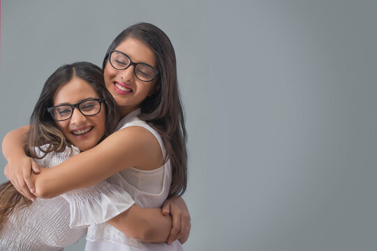 Two smiling young girls in spectacles hugging each other with eyes closed