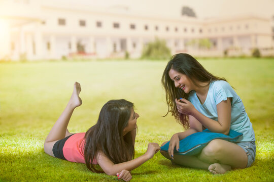 Two girls in a park talking to each other with a building in background.