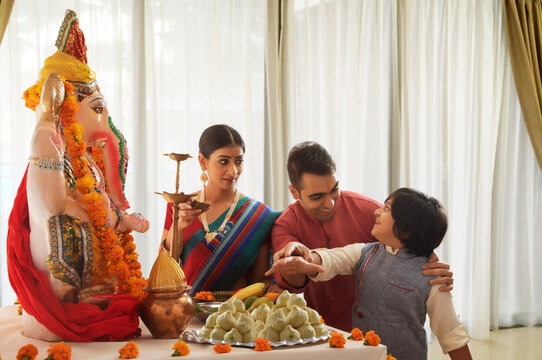 Nuclear family perparing for ganpati pooja where son tries to eat the prasad and the father stops him