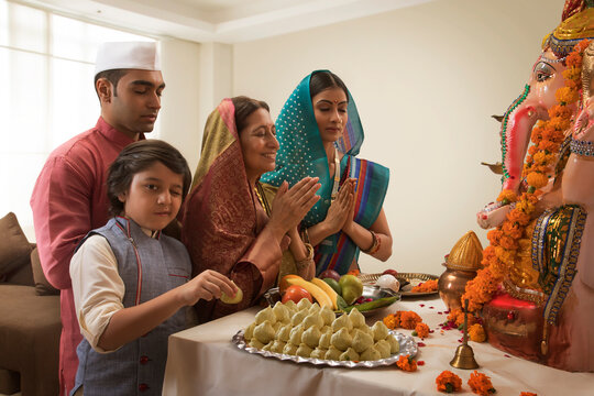 Family praying on Ganesh Chaturthi folding hands where the child winks and takes a modak from the prasad