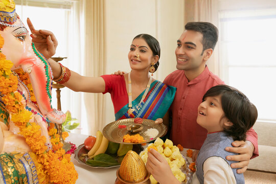 Nuclear family performing ganpati pooja and mother applying tika to the ganpati idol.