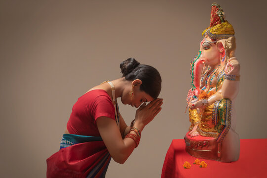 Woman praying with hands joined and eyes closed in front of Ganpati Idol.