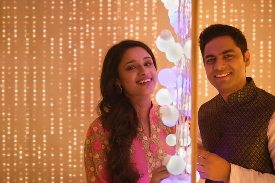 Husband and wife posing standing next to diwali lights