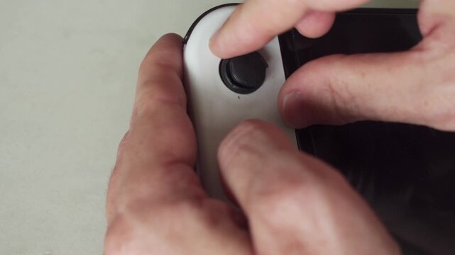 A straight on view of a man's hand manipulating a broken thumb stick on a controller where the rubber rim has broken off, on a hand held gaming device.
