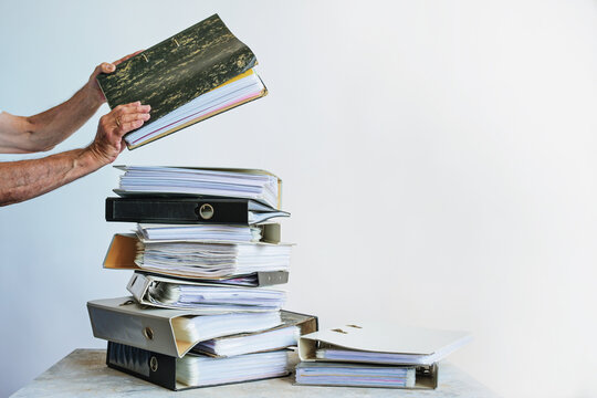 Man places a ring binder on a stack of file folders with documents, concept for overwhelming bureaucracy in a business, including office work, accounting and bookkeeping, copy space