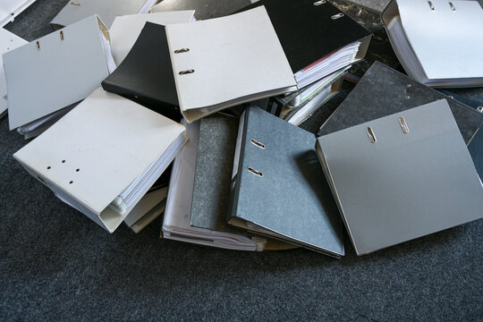 Lots of ring binders are scattered on a gray carpet in the office, symbolizing excessive bureaucracy and business record-keeping requirements, top view from above