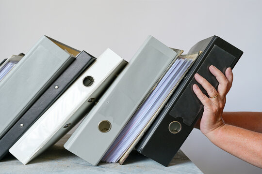 Helping hands holding a slanted row of ring binders just before falling over, business concept for assistance with bookkeeping, finances, accounting and taxes