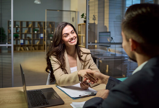Client advisor handshake during meeting and contract. Smiling woman finalizes terms with banker or broker, discussing consultation details across desk. Concept of strong business agreement.