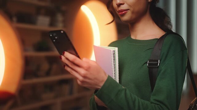 Positive female student scrolling through book reviews on phone in library