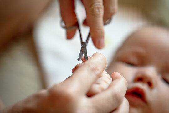 Mother cutting fingernails of newborn baby using small scissors at home
